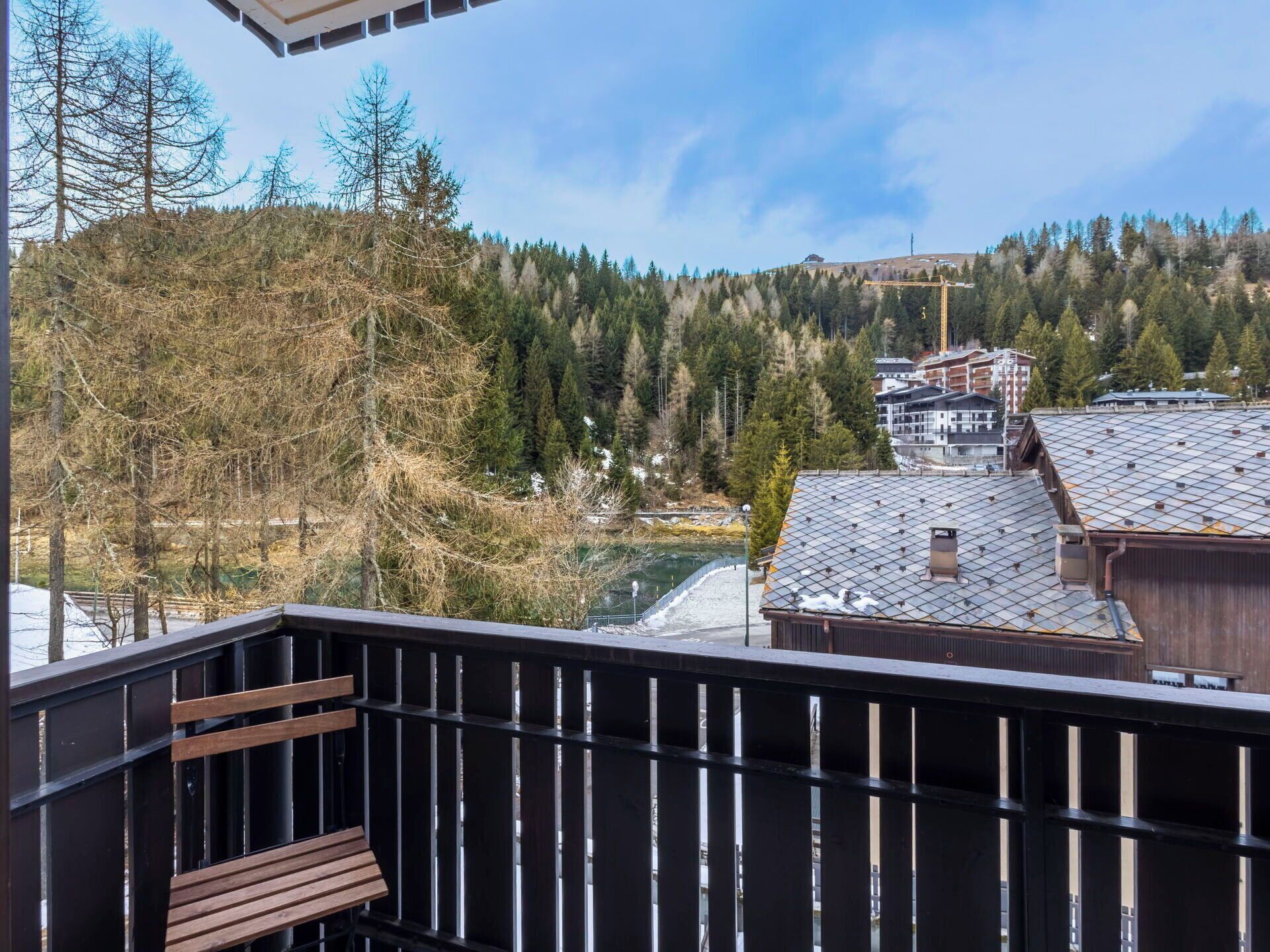 A balcony with a view of a forested hillside and buildings in the background.