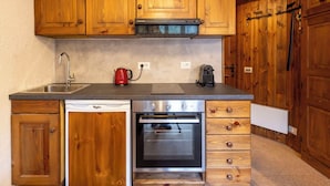Eine Küche mit Holzausstattung, einem Edelstahlspülbecken, einer roten Kaffeemaschine, einem Geschirrspüler und einem eingebauten Backofen.
