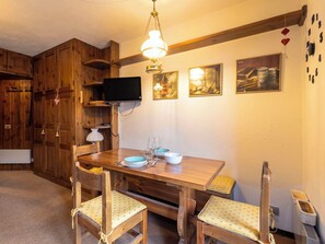 Ein Essbereich mit Holzboden, ein Tisch für vier Personen, ein an der Wand befestigter Fernseher und gerahmte Kunstwerke darüber.