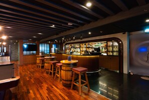 A bar area with wooden floors, stools, and a bar counter with shelves of bottles. - The First Collection Marina (Dubai)