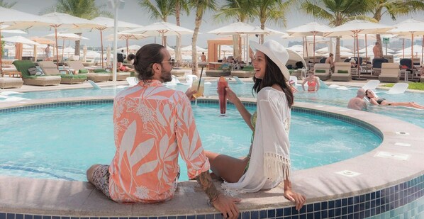 A poolside area with lounge chairs and umbrellas, a hot tub, and a view of the pool. - The First Collection Marina (Dubai)