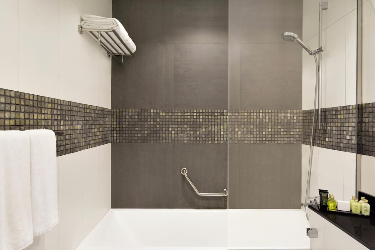 A modern bathroom with a bathtub, a shower, a handrail, and a towel rack.