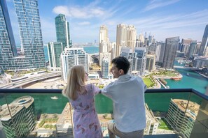 A couple overlooking a cityscape with modern high-rise buildings, a marina, and a body of water. - The First Collection Marina (Dubai)