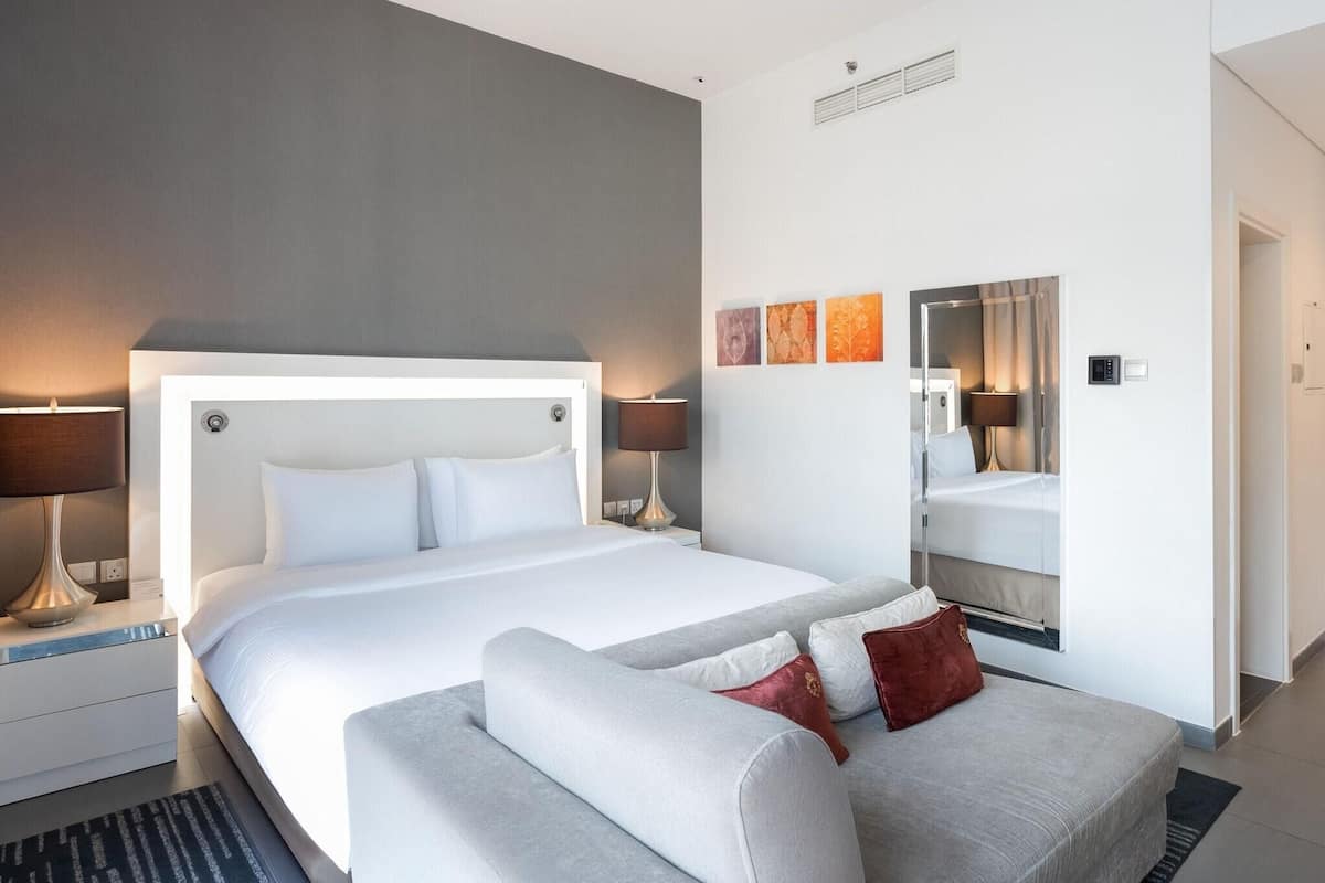 A modern hotel room with a large bed, bedside lamps, a sofa, and a mirror.
