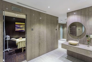 A modern treatment room with a massage table, a large mirror, and a sink with a bowl basin. - The First Collection Marina (Dubai)