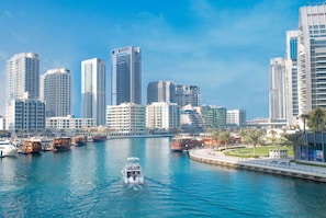 A waterfront cityscape with high-rise buildings, a marina with boats, and a promenade with palm trees. - The First Collection Marina (Dubai)