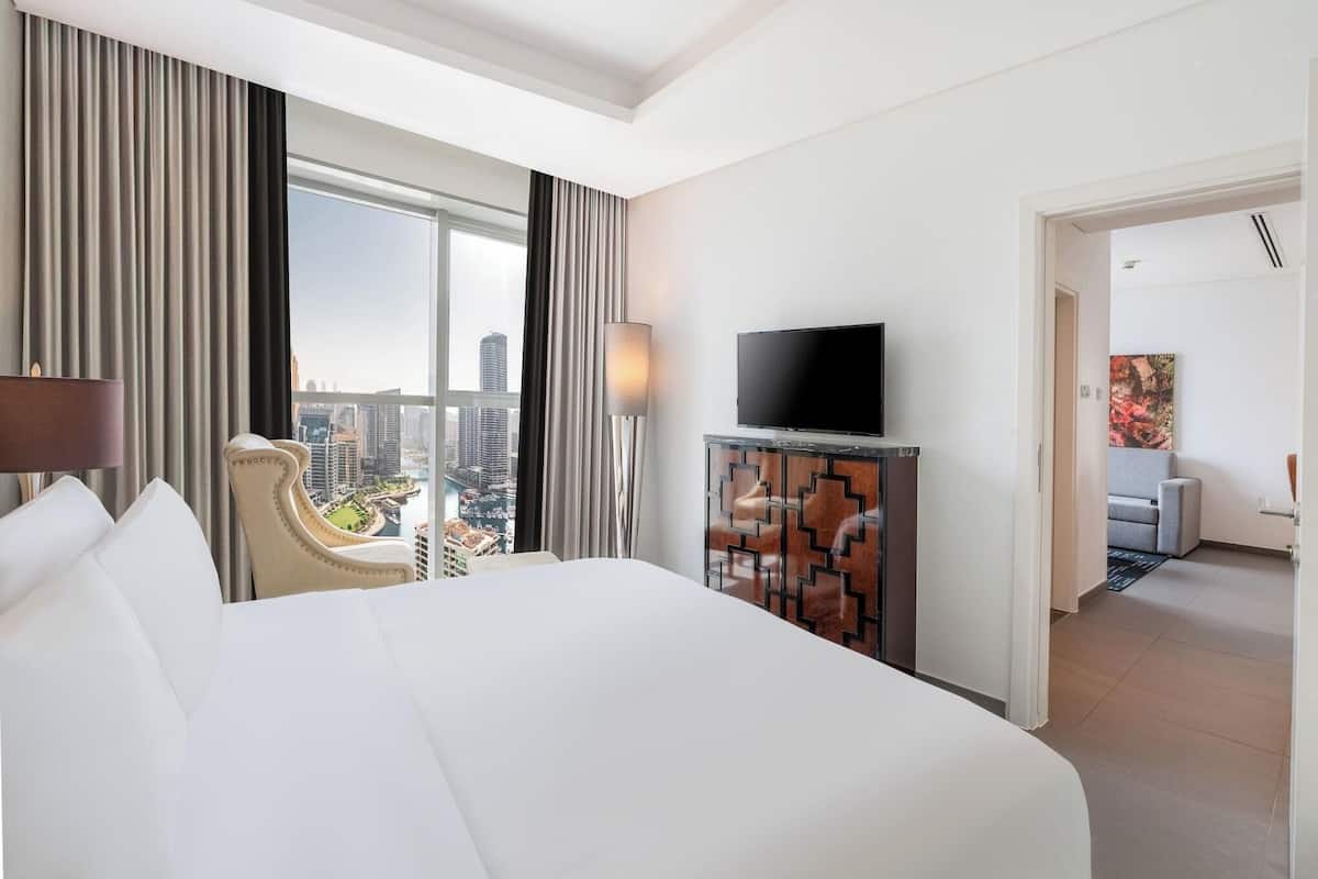 A hotel room with a large bed, a television, a view of the city, and a modern decor.