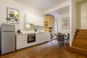 Une cuisine moderne avec des meubles blancs, un four encastré et un coin repas comprenant une table et des chaises.