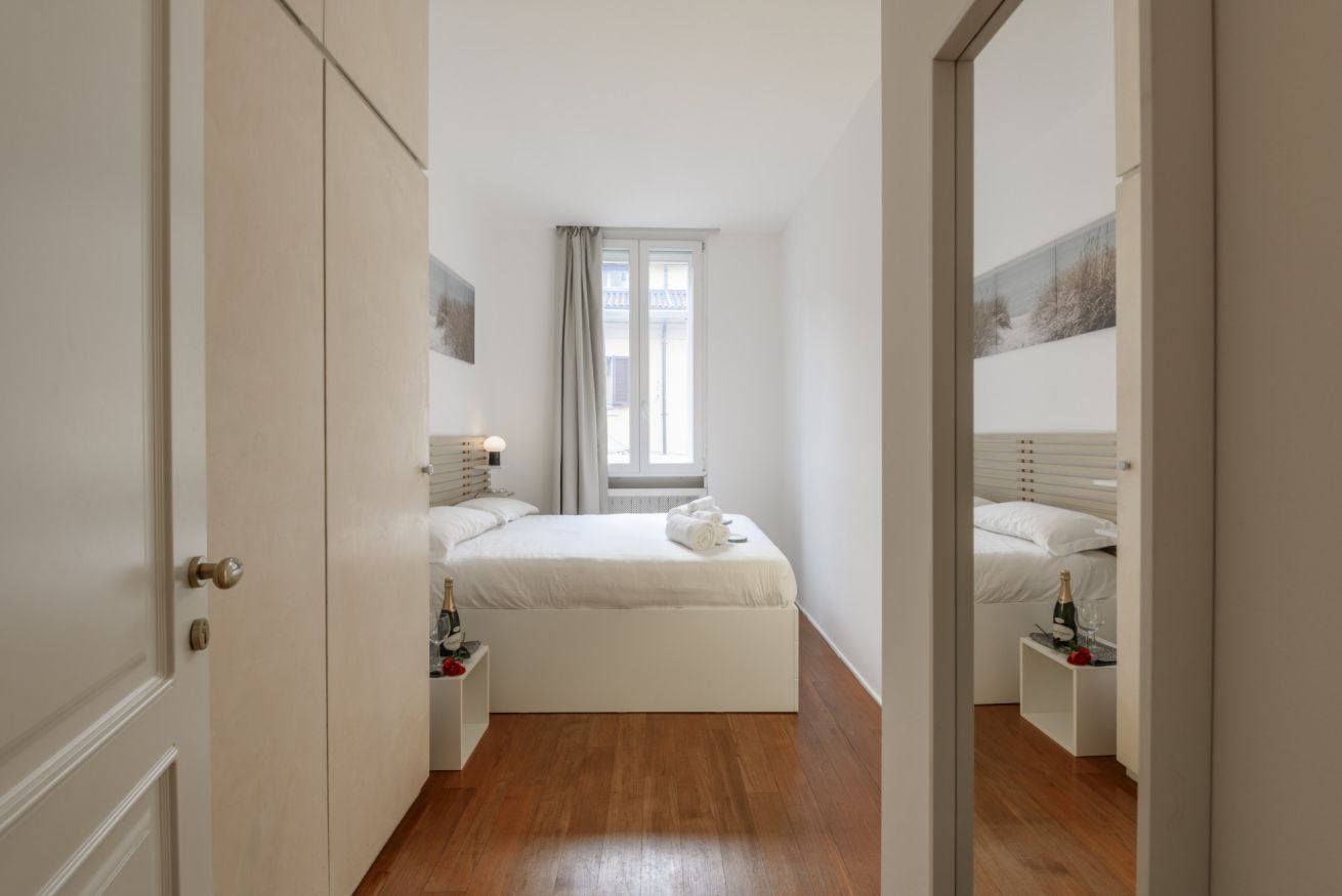 Un dormitorio con cama, mesitas de noche, una ventana y una puerta.