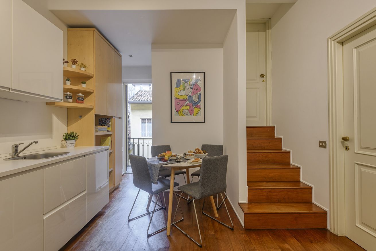 A compact kitchen with a dining area, wooden staircase, and a framed artwork on the wall.
