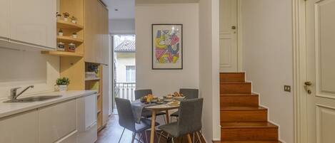 Una cocina compacta con zona de comedor, escalera de madera y una obra enmarcada en la pared.