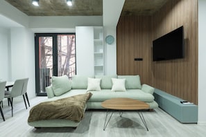 A modern living room with a sofa, coffee table, and a television mounted on a wooden wall. - Bright 1BR apartment in Avlabari (Tbilisi)