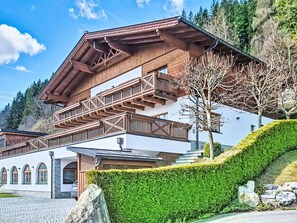 Ein mehrstöckiges Holzhäuschen mit Balkonen, einer Steinfassade und einer Bergkulisse.