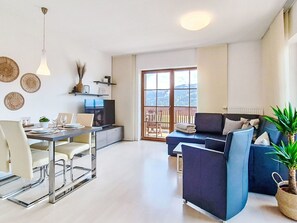 Ein modernes Wohnzimmer mit Essbereich, Fernseher und Balkon mit Aussicht.
