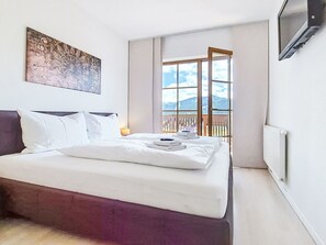 Ein Hotelzimmer mit Bett, einem Gemälde, einem Fenster mit Bergblick und einem Fernseher.