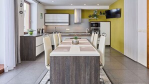 A modern kitchen with a dining area, featuring a central island, white cabinets, and a flat-screen TV mounted on the wall. - Cosy apartment for 6 guests with WIFI, TV and terrace (Turnov)