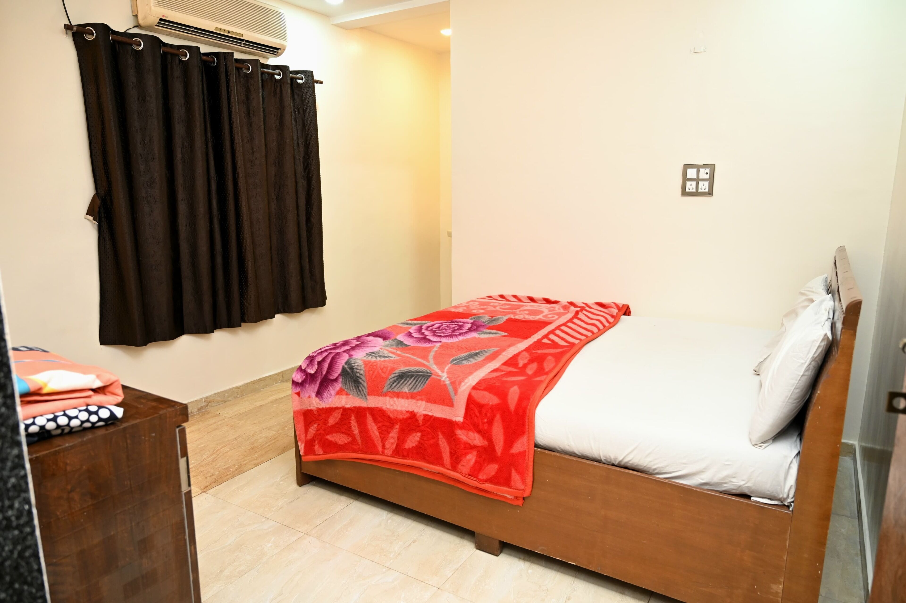 Un dormitorio con una cama de madera, una colcha floral roja y cortinas negras.