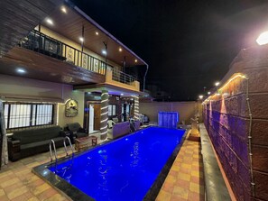 Una piscina con revestimiento azul, rodeada por un suelo a cuadros y un balcón con barandilla.