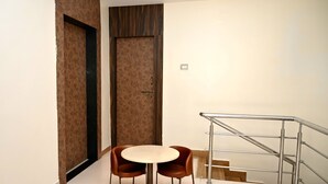 Ein kleiner Raum mit einem runden Tisch und zwei Stühlen, einer Tür mit Muster und einer Treppe mit Metallgeländer.