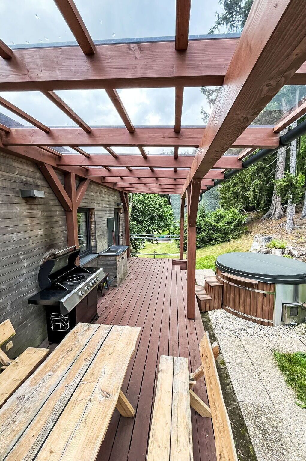 An outdoor patio with a wooden deck, a grill, and a hot tub.