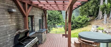 An outdoor patio with a wooden deck, a grill, and a hot tub.