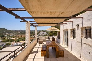 A balcony with a wooden table and chairs, a pergola, and a view of a town and hills. - Apartment No. 6, 1 bedroom, 1 bathroom (Cala Llonga)