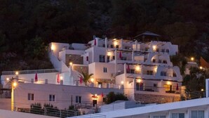 A multi-story hotel with balconies, a stone facade, and a mountainous backdrop. - Apartment no. 6, 1 bedroom, 1 bathroom (Cala Llonga)