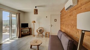 A living room with a wooden wall, a sofa, a TV, a lamp, and a chair. - Apartment no. 6, 1 bedroom, 1 bathroom (Cala Llonga)