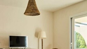 Een woonkamer met een televisie, een rieten lamp, een rieten stoel, een ronde salontafel en een bank.