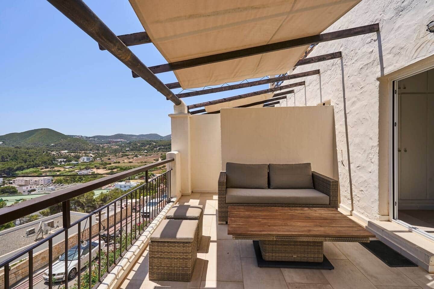A balcony with a sofa and a table, a view of the city, and a mountain in the background.