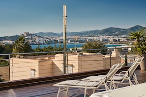 Une terrasse sur le toit, dotée de chaises longues, offrant une vue sur le paysage urbain de la côte et un ciel dégagé.
