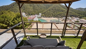 Eine Holzterrasse mit einer Couch und einem Tisch, mit Blick auf einen Strand und Gebäude.