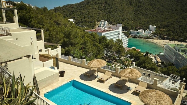 Ein Pool auf dem Dach mit Liegestühlen und Sonnenschirmen, umgeben von einer Berglandschaft und einem Strand.