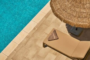 A poolside area with a lounge chair, a thatched umbrella, and a tiled deck. - Studio 1, bed for 2 persons (Cala Llonga)