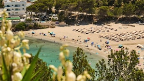 A beach with numerous umbrellas and sun loungers, surrounded by buildings and trees. - Apartment nº7, 1 bedroom, 1 bathroom (Cala Llonga)