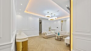 Ein geräumiges Wohnzimmer mit Fischgrätparkett, einer beigen Sofagarnitur, einem Couchtisch und einer Wand mit goldenen Akzenten.