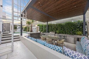 An outdoor kitchen area with a dining set, a grill, and a seating area with patterned cushions. - Luxury Villa with Pool- Cinema and Spa  (Dubai)