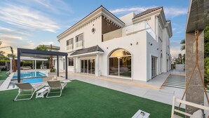 Ein modernes, zweistöckiges Haus mit Swimmingpool, Außenmöbeln und einer überdachten Terrasse.