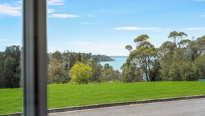 A view of a grassy area with trees and a body of water in the distance. - Lakeside 3 BDR House (Koonawarra)
