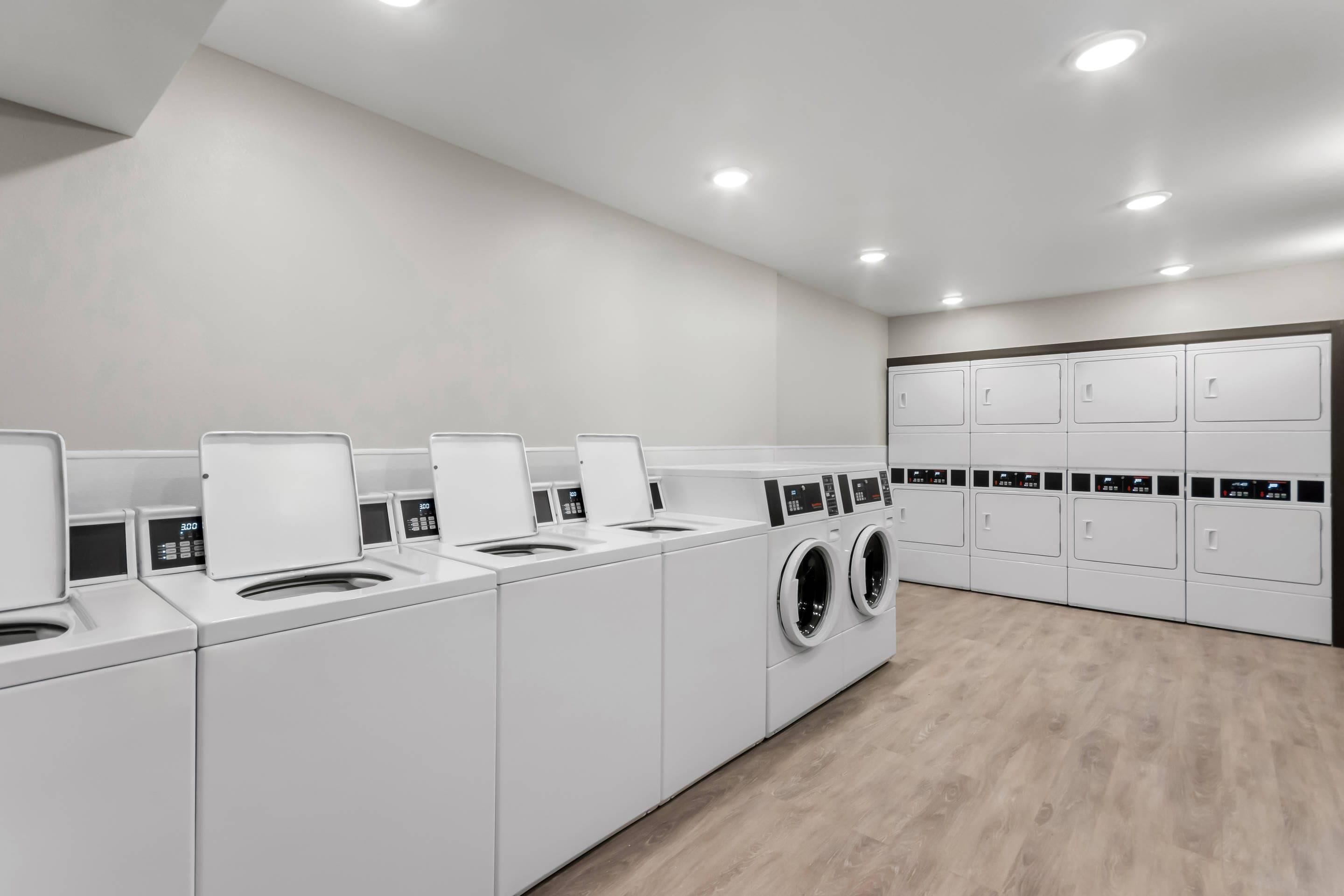 Un moderno cuarto de lavandería con varias lavadoras y secadoras, piso de madera y un diseño limpio y minimalista.