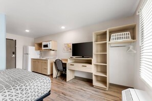 A compact room with a bed, kitchenette, desk, TV, and built-in shelving. - WoodSpring Suites Fort Walton Beach - Eglin AFB (Fort Walton Beach)