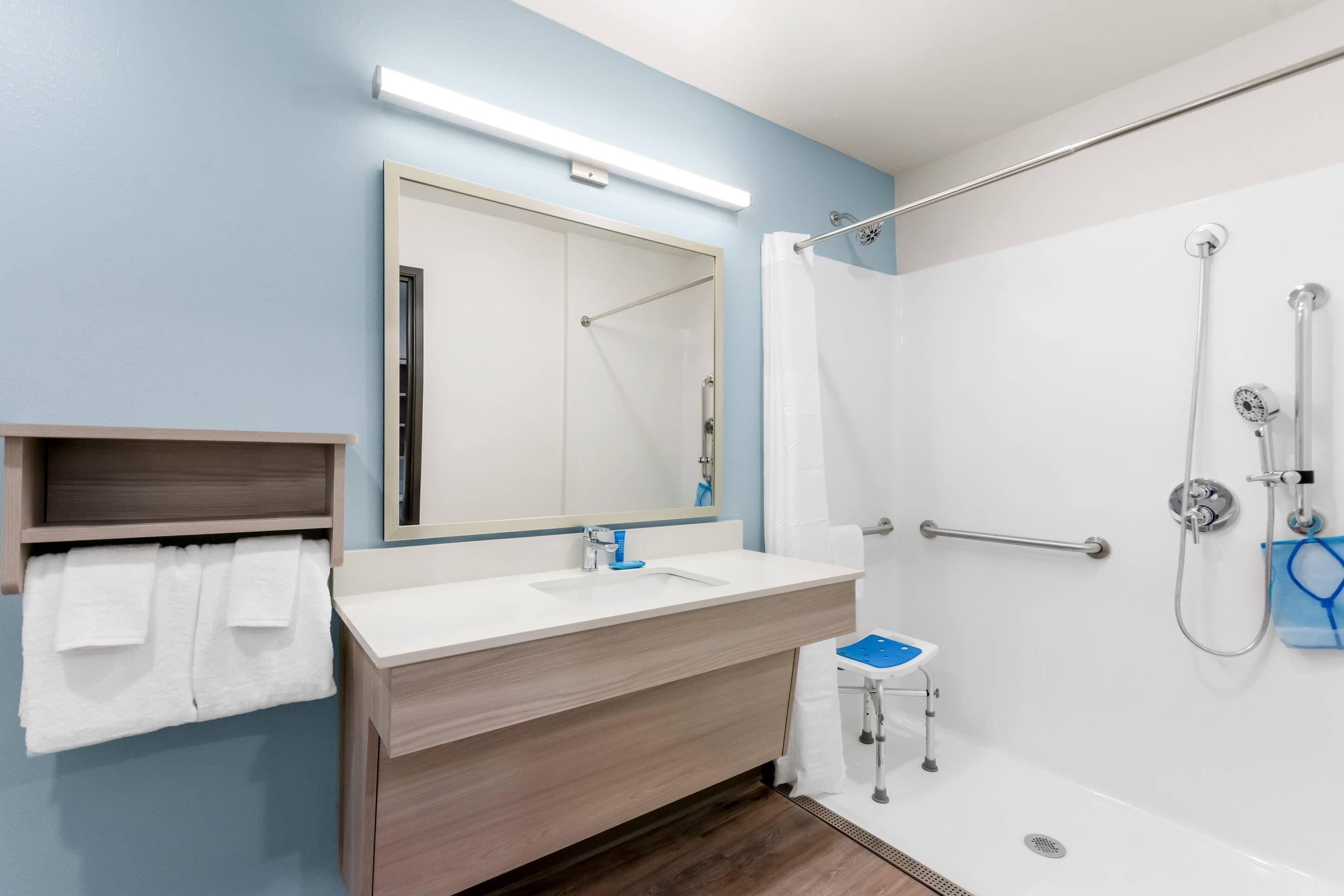 Une salle de bain moderne équipée d’une douche, d’un lavabo, d’un miroir et d’un porte-serviettes.