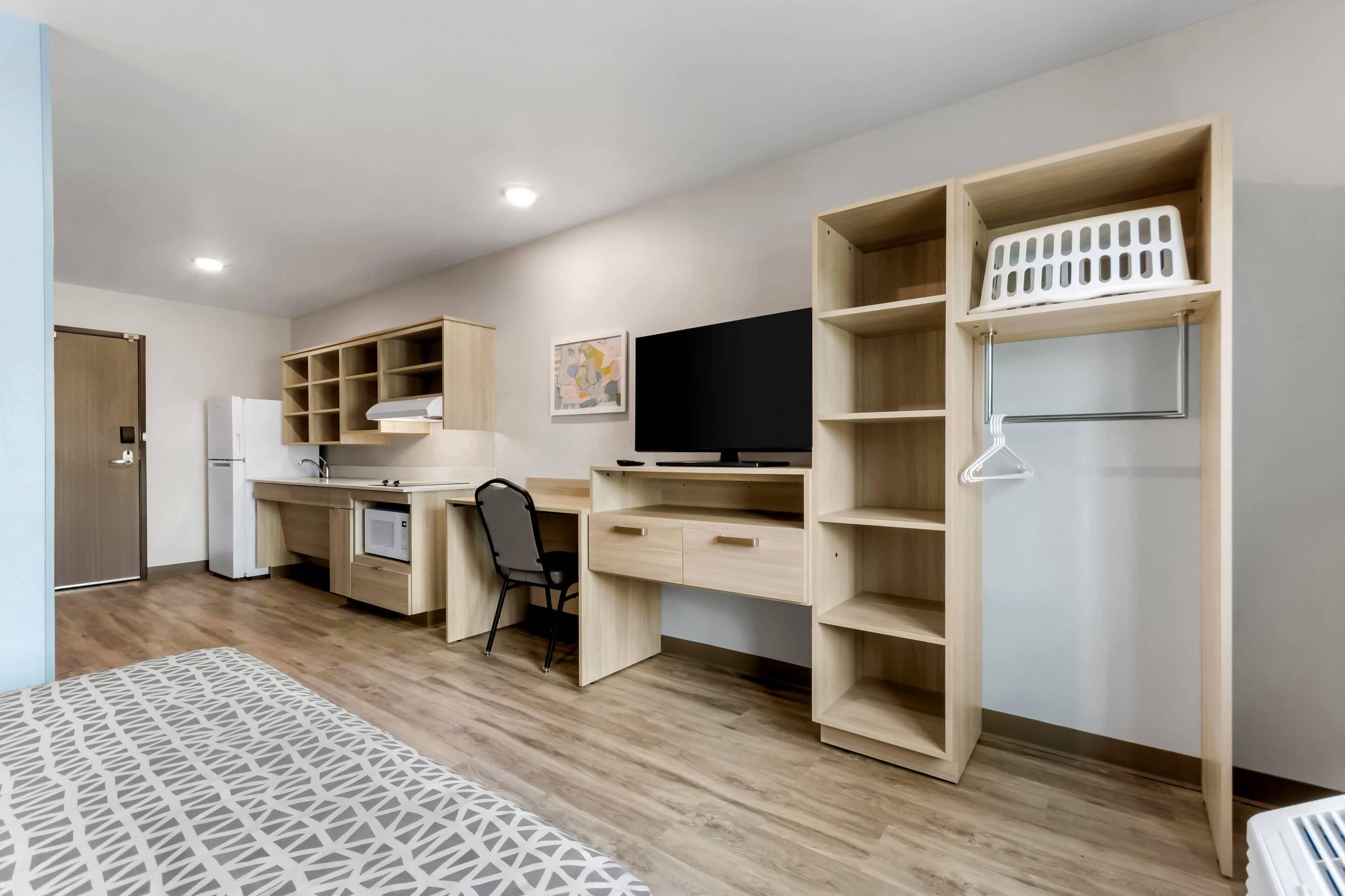 Une pièce moderne et bien éclairée, dotée d’une kitchenette, d’un bureau avec une chaise et d’étagères intégrées.