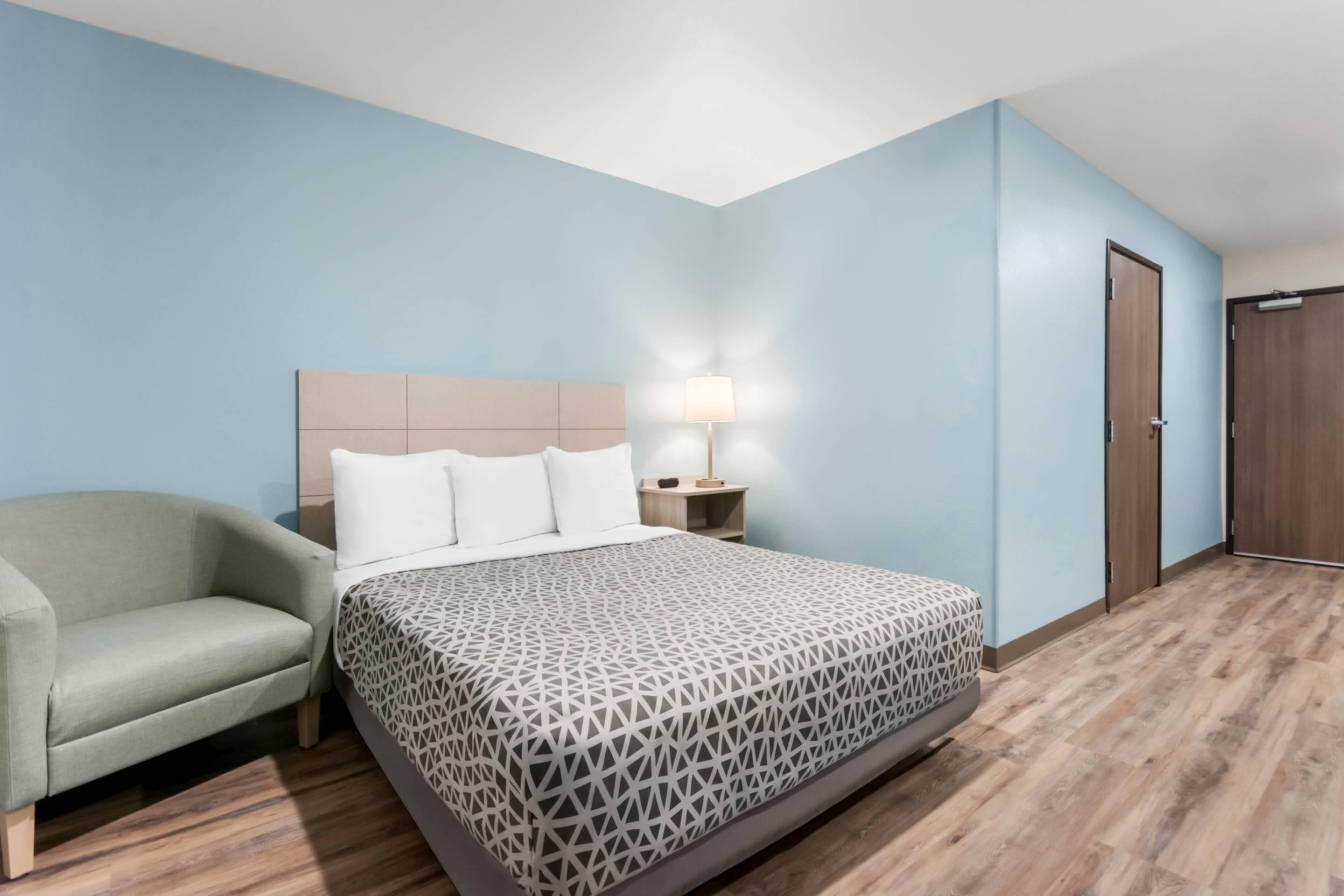 A hotel room with a bed, a nightstand, a lamp, a chair, and a wardrobe.