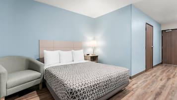 A hotel room with a bed, a nightstand, a lamp, a chair, and a wardrobe.