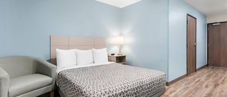 A hotel room with a bed, a nightstand, a lamp, a chair, and a wardrobe.