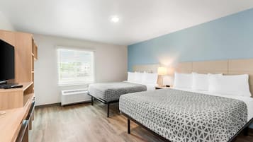 A hotel room with two beds, a desk, a TV, a window with blinds, and a lamp.
