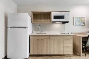 A compact kitchen with a built-in refrigerator, a microwave, and a sink. - WoodSpring Suites Fort Walton Beach - Eglin AFB (Fort Walton Beach)