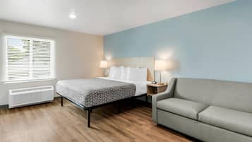 Una habitación de hotel con cama, lámparas de noche, calefacción, sofá y ventana con persianas.