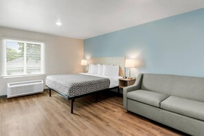 Ein Hotelzimmer mit einem Bett, Nachttischlampen, einem Heizgerät, einem Sofa und einem Fenster mit Jalousien.